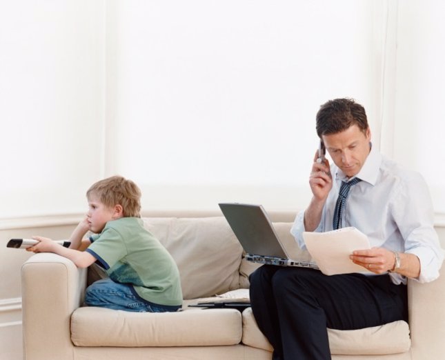 Padre ocupado con móvil y ordenador e hijo aburrido